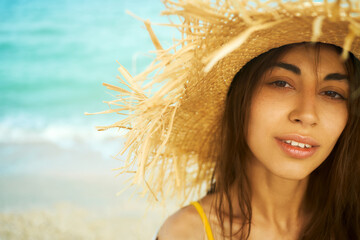Wall Mural - close-up face beautiful traveler woman in straw hat at beach by ocean. looking to camera and relaxing at beach. summer holiday vacation