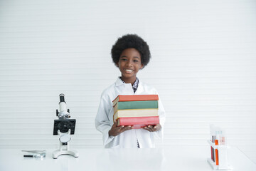 Little African kid boy scientist smile and holding many text books with a microscope and various colorful flasks test tube at laboratory on a white background