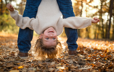 Wall Mural - Unrecognizable father holding small daughter upside down in autumn forest.