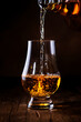 Scotch Whiskey without ice pouring out of the bottle, rustic wood background, copy space