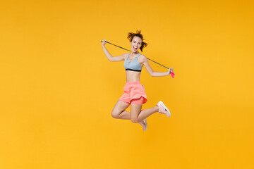 Wall Mural - Full length portrait excited young fitness woman in sportswear working out isolated on yellow background. Workout sport motivation lifestyle concept. Mock up copy space. Jumping, hold skipping rope.