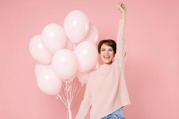 Happy young brunette woman girl in knitted casual sweater posing isolated on pastel pink background. Birthday holiday party people emotions concept. Celebrating hold air balloons doing winner gesture.