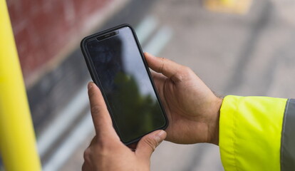 Architect holding a smartphone on construction site - young construction worker is using mobile phone on site - Construction worker with building plans and cellphone - Focus on mobile. warm filter