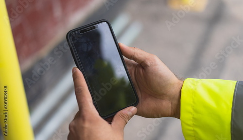 construction man holding a mobile on site. Man pointing on smartphone screen, chatting in social networks, site meeting, social distancing, meeting website and sending sms, text messenger on site.