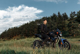 Fototapeta  - Handsome biker sitting on motorcycle in sunset on the country road.