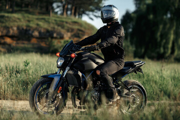 Photo of biker sitting on motorcycle in sunset on the country road.