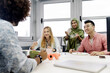 © Santi Nunez/Stocksy - multinational team concept. A Muslim woman in a hijab, a Caucasian woman and an asian guy taking a break for lunch in the office. Coworking concept.