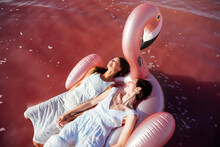 Beautiful Young Women Lying On Pelican Inflatable Mattress On Pink Sea