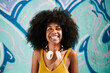 © MyMicrostock/Stocksy - Happy afro woman looking at camera besides a graffiti wall