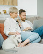 © Duet Postscriptum/Stocksy - Young beautiful couple with dog sitting on the sofa using laptop at new stylish home