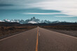 © EZ PHOTOS - Panoramic image of a long straight asphalt road leading to frozen snowy mountains in the horizon and some clouds in the blue sky. Patagonia, Chile.