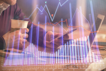 Double exposure of man's hands holding and using a phone and financial graph drawing. Analysis concept.