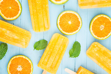 Wall Mural - Homemade frosty popsicles with oranges on a blue wooden background