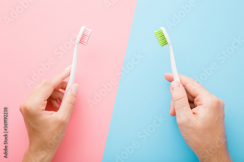Young man and woman hands holding toothbrushes on blue pink table background. Pastel colors. People teeth hygiene. Living together concept. Closeup. Top down view.