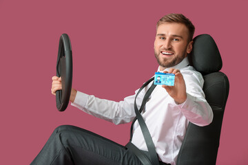 Canvas Print - Young businessman with steering wheel and driving license sitting on car seat against color background