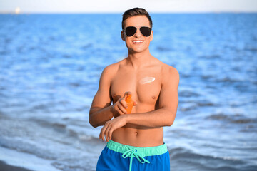 Sticker - Handsome young man applying sunscreen cream on sea beach