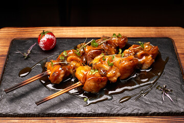 Rapana shish kebab with teriyaki sauce and romidor, on black slate, on a wooden board