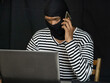 © think4photop - Ski Masked hacker with mobile smart phone and laptop stealing important information data.