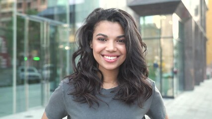 happy stylish young mixed race gen z girl wearing tshirt standing on city street looking at camera, 