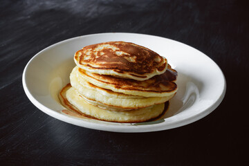 Stack of pancakes in white plate on dark table