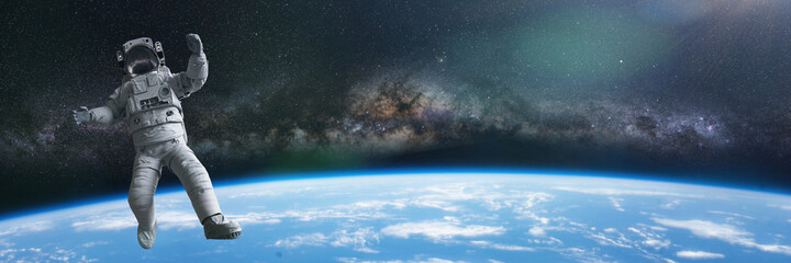 Wall Mural - astronaut during a spacewalk in orbit of planet earth, background banner with empty space