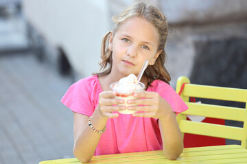 Canvas Print - beautiful girl in a pink t-shirt sits at a yellow table and eats ice cream