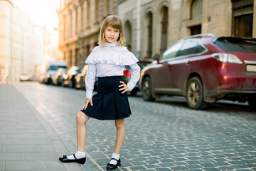 Full length portrait of beautiful little blond girl outdoors at old city street in Lviv, Ukraine. Fashion strret portrait of pretty girl in the city