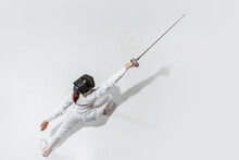 Champion. Teen Girl In Fencing Costume With Sword In Hand On White Background. Top View. Young Female Model Practicing And Training In Motion, Action. Copyspace. Sport, Youth, Healthy Lifestyle.