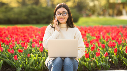 Wall Mural - Female student using phone and laptop, sitting on parapet