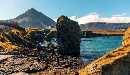 Leinwandbilder - Famous Icelandic view. basalt rocks formation on coastline with beautiful hous and Mountain Stapafell in the background at Arnarstapi Village in summer sunny day in Iceland. Amazing nature of Iceland
