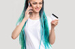 © golubovy - Z generation woman with blue colored hair braids. Cheerful lady verifying credit card personal data on mobile phone isolated on white. Banking operation. Cashless payment. Call center.