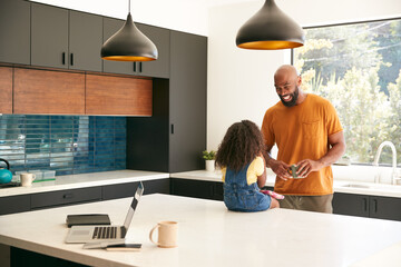 Father With Daughter Sitting On Kitchen Counter At Home Using Digital Tablet