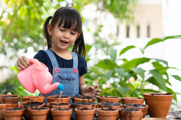 adorable 3 years old asian little girl is watering the plant in the pots outside the house, concept 