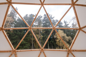 Interior of large geodesic wooden dome tent with window and view to forest. Empty interior glamping tent.