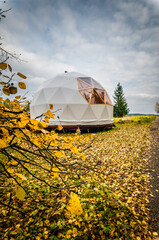 Large geodesic dome tent in autumn forest. Modern outdoor glamping tent on meadow.