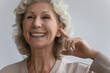 © fizkes - Close up image elderly woman point finger to ear feels happy by new modern comfort hearing aid device. Age related hearing loss, services of clinic ad for old patient diagnosis and treatment concept