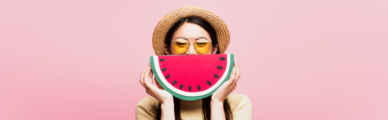 Sticker - website header of asian girl in sunglasses and straw hat covering face with paper watermelon isolated on pink