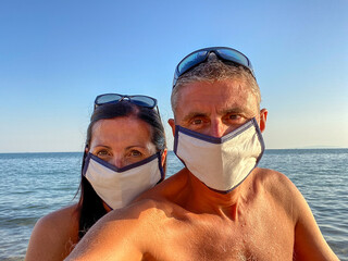 Wall Mural - Man and woman taking selfie on the beach wearing masks