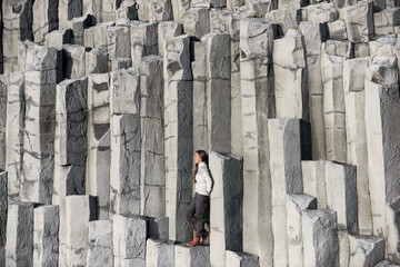 Wall Mural - Iceland tourist at beach sitting on basalt columns on Reynisfjara beach, the black sand beach of Vik, South Iceland coast. Happy woman visiting tourist attraction destination.