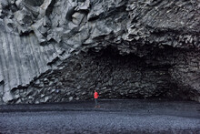 Iceland Tourist Woman Walking On Reynisfjara Black Sand Beach By Basalt Columns And Cave, Beach Of Vik, South Iceland Coast. Happy Woman Visiting Tourist Attraction Destination.
