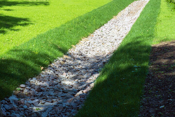 drainage, a drainage system in a Park area, a waterway overgrown with lawn and paved with stones, an Aqueduct between nature and the road. stone water drains in a grass garden field. Lawn and plant