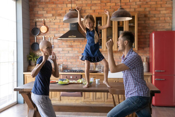 Wall Mural - Happy young Caucasian family with little child with ill cancer patient hairless mom have fun at home kitchen together, smiling dad and small daughter entertain sick bald mother, dance on weekend