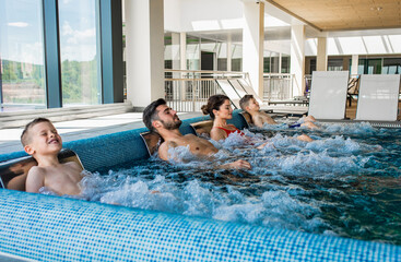 Wall Mural - smiling family of four having fun and relaxing in indoor swimming pool at hotel resort.