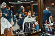 © Svitlana - Young guy sitting in barbershop chair in front of the mirror and getting new haircut. Young professional barber girl working with hair clipper
