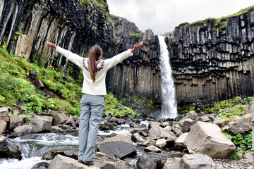 iceland. woman enjoying majestic svartifoss waterfall. female is visiting famous tourist attraction 