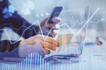 Double exposure of man's hands holding and using a phone and financial graph drawing. Analysis concept.