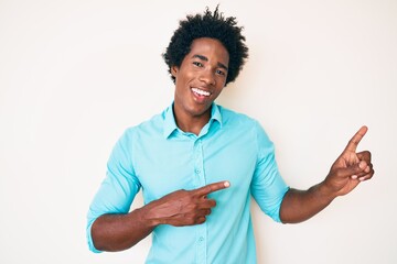 Handsome african american man with afro hair wearing casual clothes smiling and looking at the camera pointing with two hands and fingers to the side.