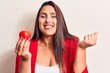 © Krakenimages.com - Young beautiful brunette woman holding tomato screaming proud, celebrating victory and success very excited with raised arm