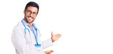 Young Hispanic Man Wearing Doctor Uniform And Stethoscope Inviting To Enter Smiling Natural With Open Hand