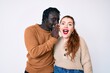 © Krakenimages.com - Interracial couple wearing casual clothes hand on mouth telling secret rumor, whispering malicious talk conversation